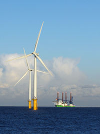 Windmills by sea against sky