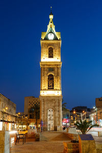 Illuminated clock tower amidst buildings in city at night