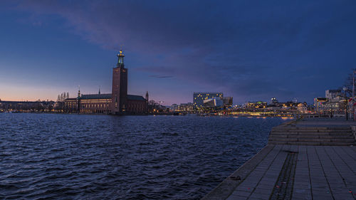 Illuminated buildings by river against sky in city