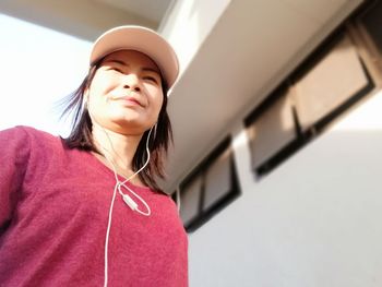 Smiling woman wearing in-ear headphones while standing against building 