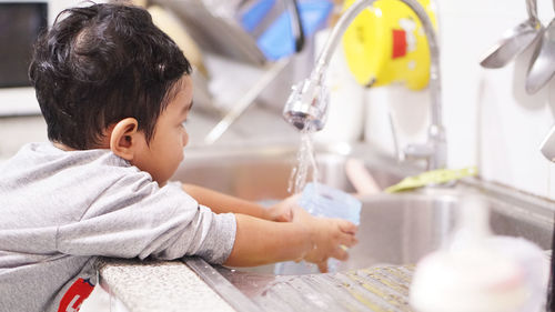 Rear view of boy drinking water from faucet