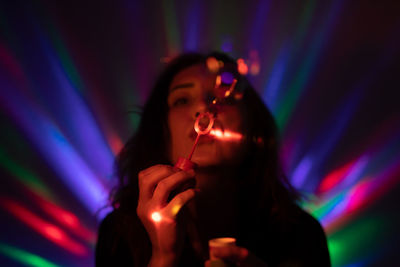 Woman blowing bubbles against illuminated lights