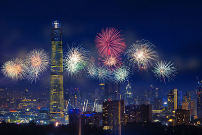 Firework display in city against sky at night