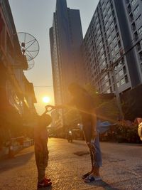 People on street amidst buildings in city during sunset