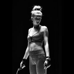 Portrait of young woman standing against black background