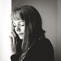 Young woman with eyes closed standing by wall