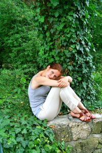 Side view portrait of young woman hugging knees while sitting by plants
