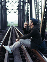 Side view of young man sitting on railroad track