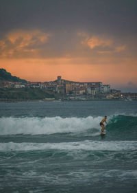 Man surfing in sea against sky during sunset