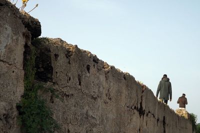 Low angle view of man standing on rock against sky