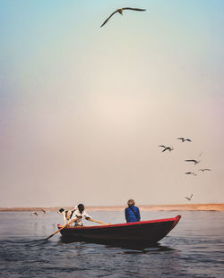 People sitting in boat over sea against flying birds