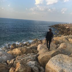 Rear view of woman standing on rock by sea against sky