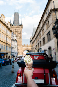 Cropped hand holding ice cream against buildings in city