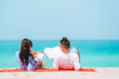 Woman sitting on beach against clear sky