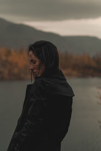 Woman standing by lake against sky during sunset