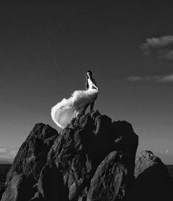 Low angle view of mid adult woman standing on rock against sky