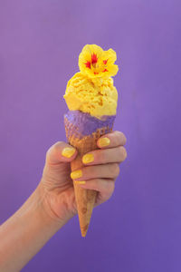 Cropped image of hand holding ice cream against colored background