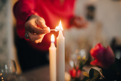 Midsection of mature woman igniting candle on dining table in party at home