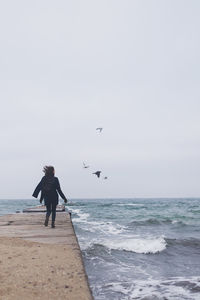 Beautiful woman walking on the beach with seagulls in winter time. free spirit concept person