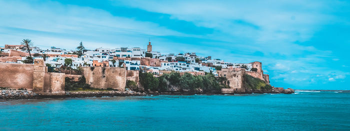 Buildings by sea against blue sky