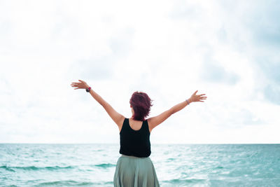 Rear view of woman standing at beach against sky