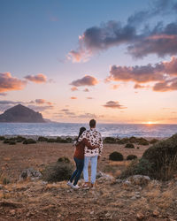 Rear view of friends standing on beach against sky during sunset