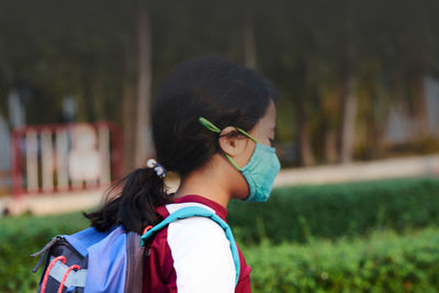 Side view of young woman looking away against trees