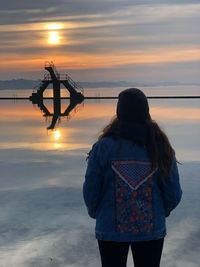 Rear view of woman standing at sea against sky during sunset