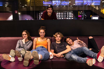 Portrait of happy multi-ethnic teenage friends on sofa at bowling alley