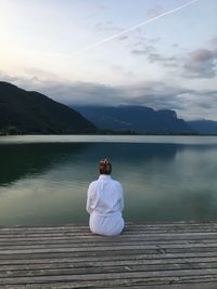 Rear view of woman sitting on pier over lake