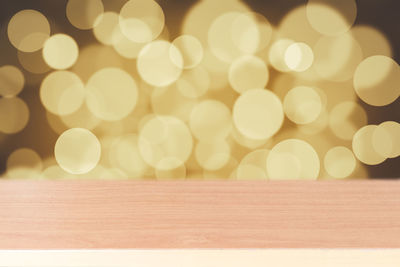 Close-up of wooden table against illuminated lights