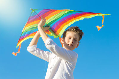 Low angle view of young woman holding flag against blue sky