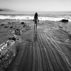 Rear view of woman walking towards sea against clear sky