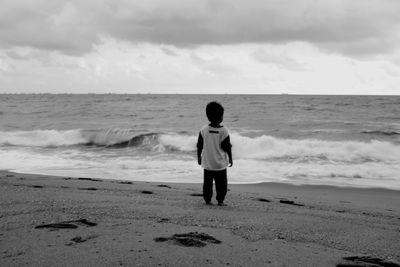 Rear view of boy standing on beach against sky