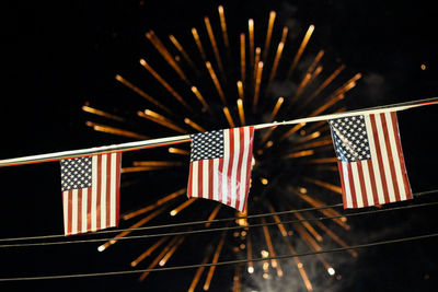 Low angle view of american flags against illuminated fireworks at night