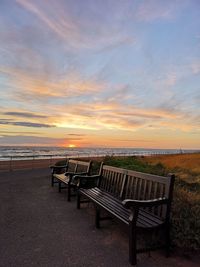 Empty benches against sea and sky during sunset