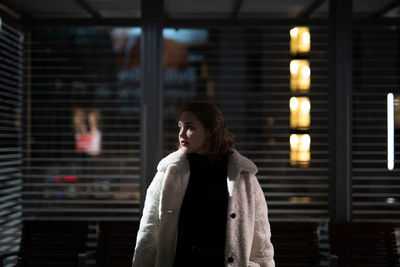 Young woman looking away while standing against window