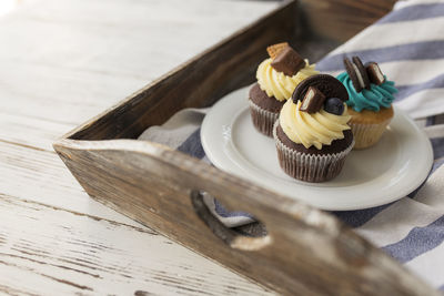 Tasty multicolored muffins and cupcakes on white plate on wooden tray with towel. decorated candies