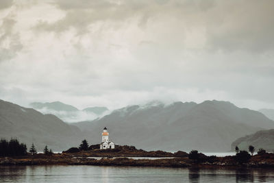 Lighthouse amidst buildings and mountains against sky