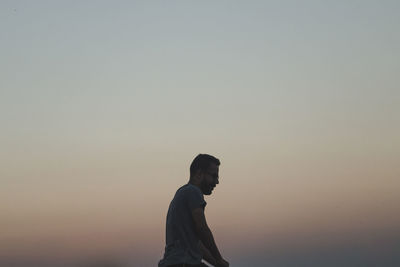 Side view of man standing against clear sky during sunset