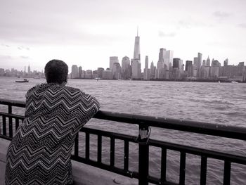Rear view of man standing by railing against buildings in city