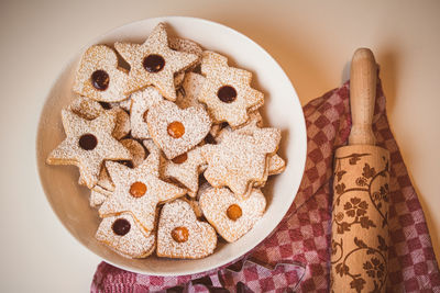 High angle view of the bowl of linzer cookies against a table cloth and a dough roller