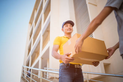 Smiling delivery man giving parcel to customer by building in city