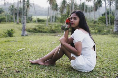 Young woman drinking water while sitting on field