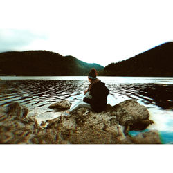 Rear view of man sitting by lake against sky