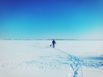 Rear view of man walking with dog on snow covered field