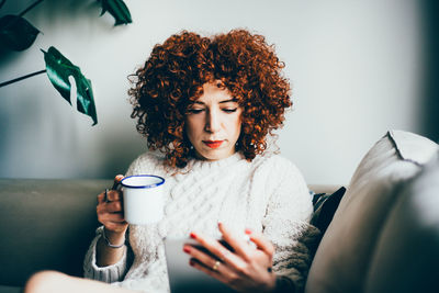 Woman using phone while having coffee at home