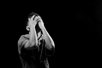 Portrait of young man covering face against black background