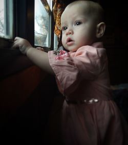 Cute baby girl looking through window at home