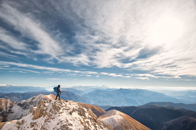 Man standing on mountain against cloudy sky during winter